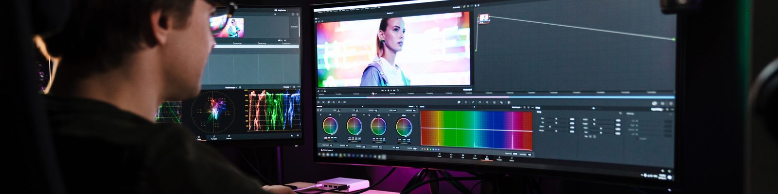 Colorist grading video on dual monitors with scopes and color wheels in a production suite