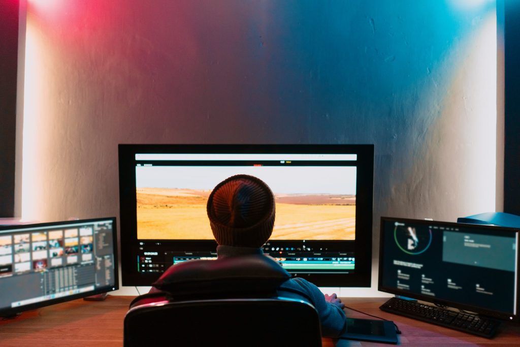 Video editor working at a workstation with a wide monitor showing footage and editing panels in a dark room